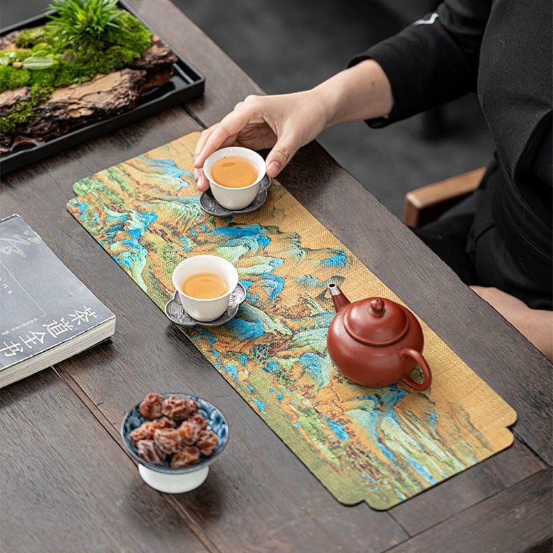 Person pouring tea on a waterproof Chinese art tea mat with a teapot and cups on a wooden table